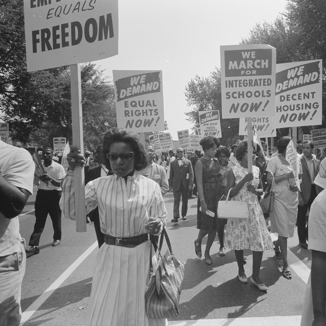 a procession of African Americans carrying signs for equal rights, integrated schools, decent housing, and an end to bias.