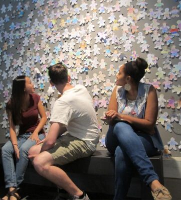 three teens sitting on a bench in front of a wall of paper cutouts
