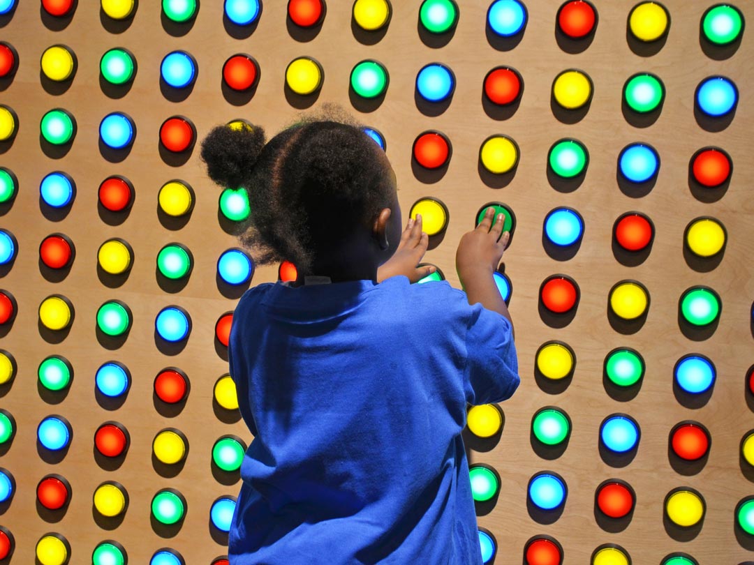 Young girl pushing large colorful buttons on a wall filled with buttons