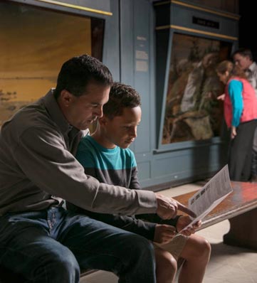 A father and son sit on a bench as the father points to something in a brochure