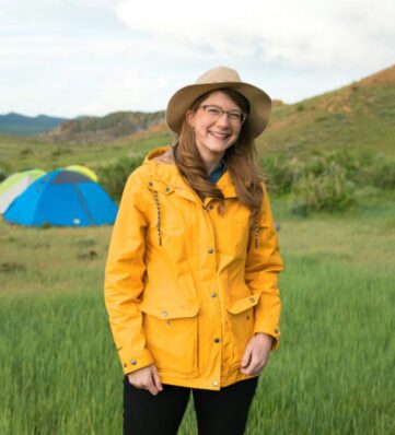 A woman standing in a field in front of tents wearing a yellow raincoat