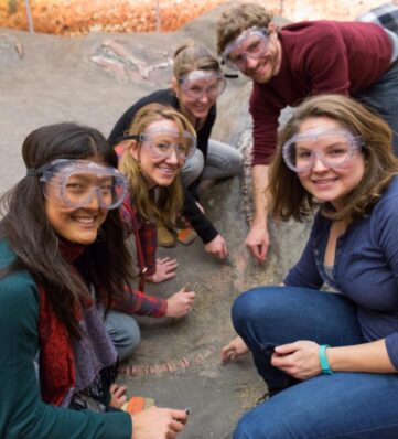 adults wearing goggles dig for dinosaur bones