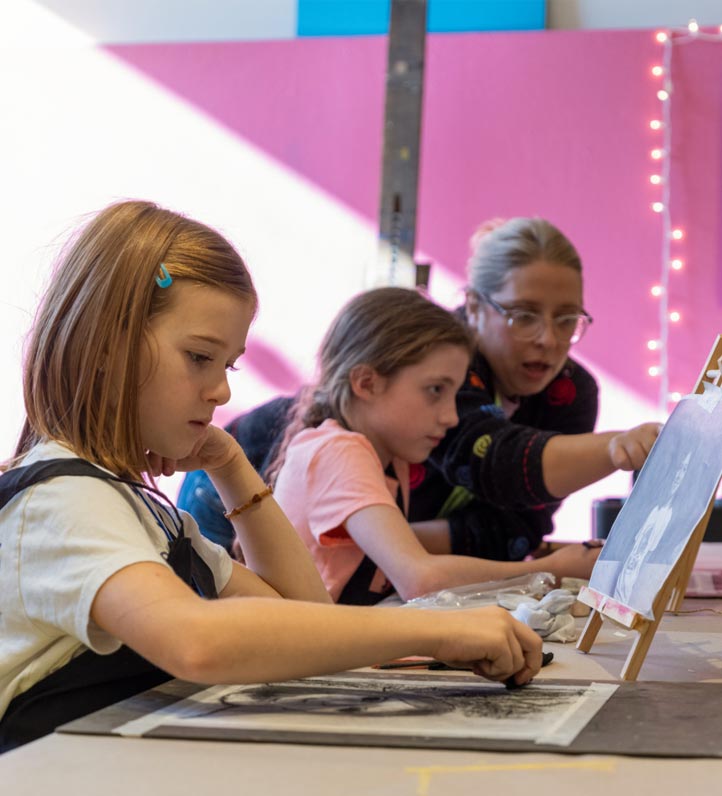 Children engaged in an art class, creating drawings with various materials on a table, set in a colorful, bright environment.