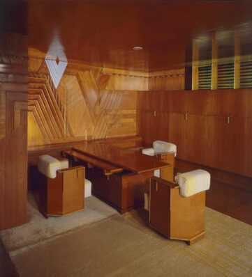 Wood-paneled interior featuring a sleek table and geometric designs with modern chairs and a warm ambiance.