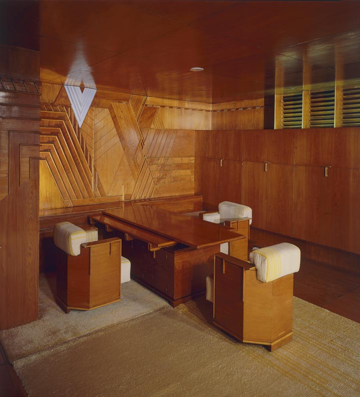 Wood-paneled interior featuring a sleek table and geometric designs with modern chairs and a warm ambiance.