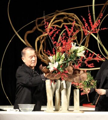 a man arranging dried flowers in tall vases with large swirls of material around him