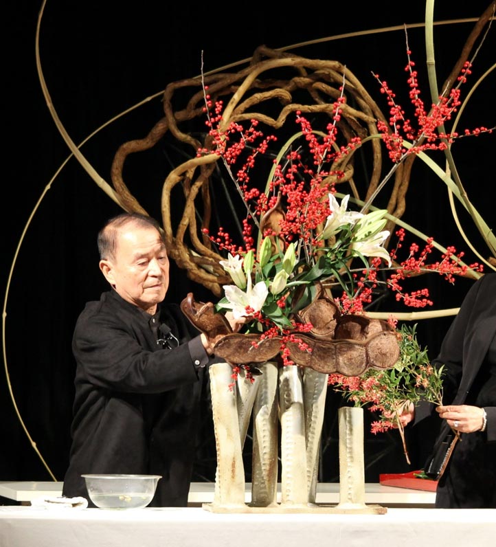 a man arranging dried flowers in tall vases with large swirls of material around him