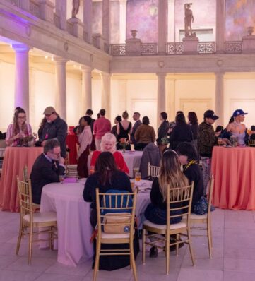 A social gathering in a spacious, elegantly decorated hall with tables, guests mingling, and vibrant floral centerpieces.