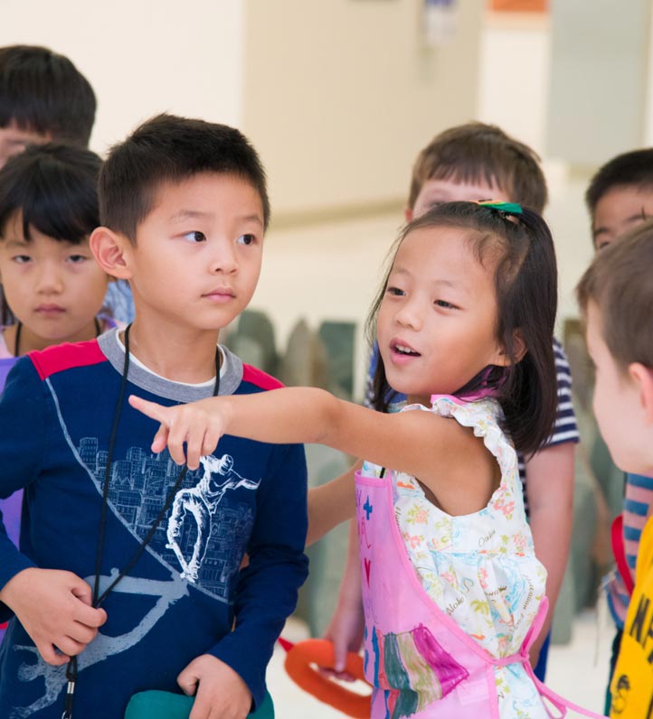A group of children engages in a playful interaction, one child excitedly pointing while others listen and observe.
