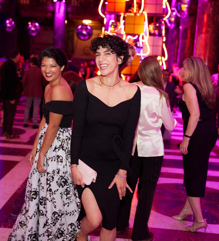 Two women in black dresses and white shoes socialize at (untitled) Art Party, surrounded by colorful artwork and festive decor.