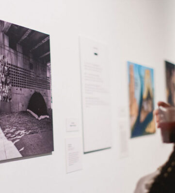 A woman in a black sweater looking at a photo on the wall of a museum