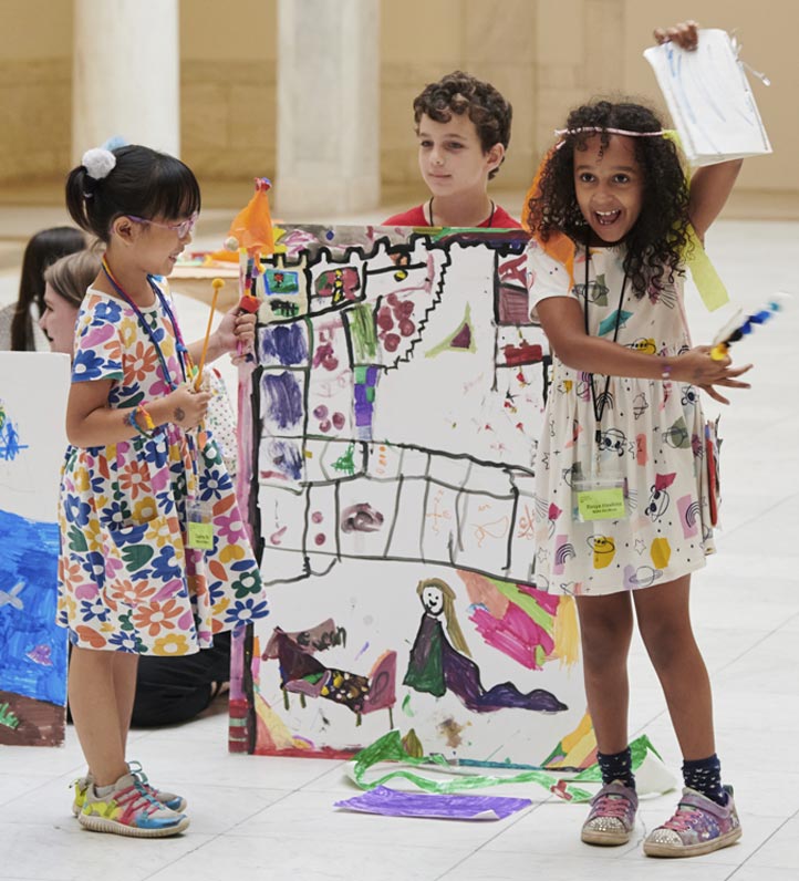 Children display their colorful artwork in a spacious indoor setting, surrounded by various creative materials.