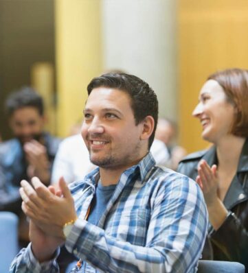 A diverse audience claps in a conference setting, showcasing engagement and enthusiasm for the ongoing presentation.