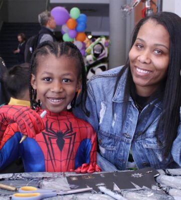 A mom with a daughter dressed as spider man do activities at a table