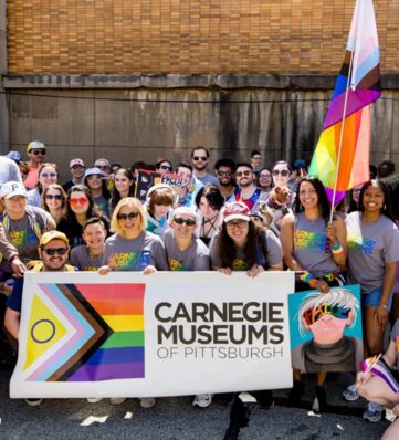 A group photo posed with a pride parade banner and flag