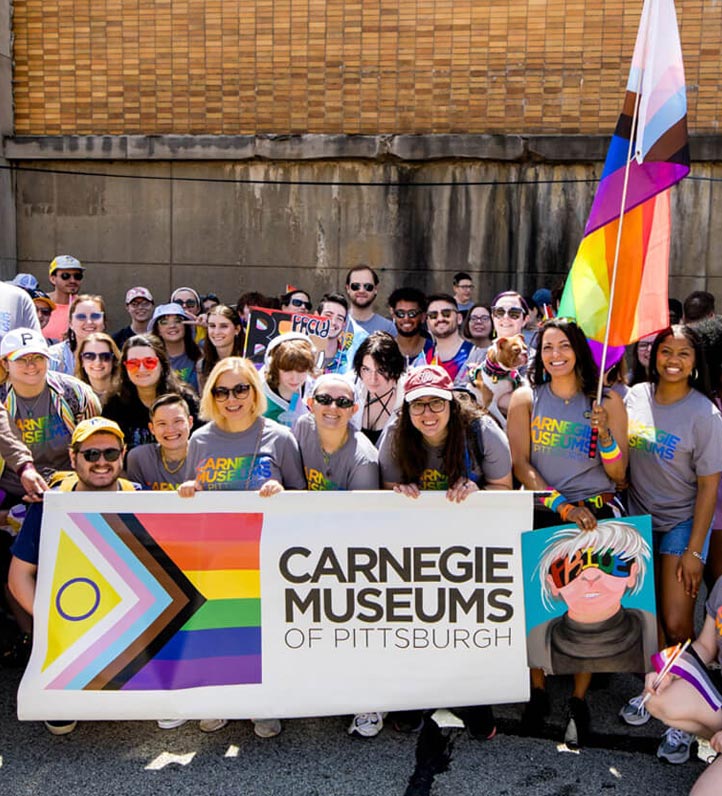 A group photo posed with a pride parade banner and flag