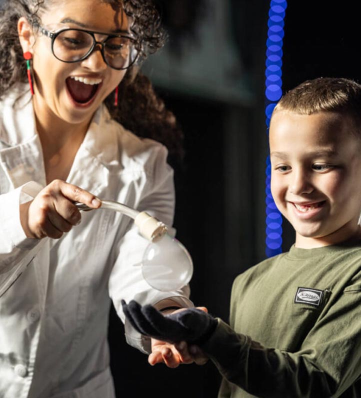 a science demonstrator produces a smoke-filled bubble in the hand of a smiling child