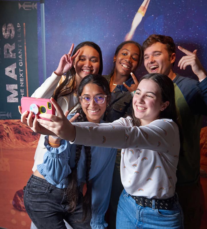 A group of teens takes a selfie in front of a colorful backdrop showcasing Mars