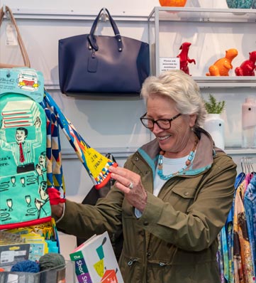 A woman examines colorful items in a store, surrounded by plush toys, bags, and decorative products. Bright and cheerful display setup.