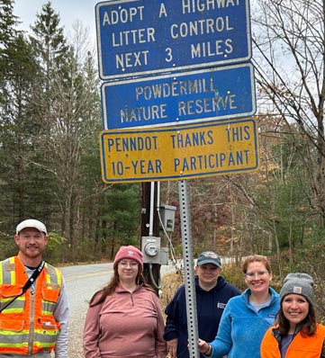 people in orange vests stand near a litter control sign
