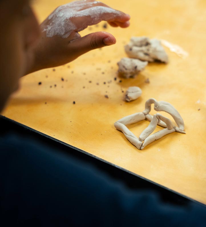 a childs hands working with clay on a yellow tabletop
