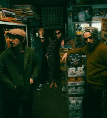 Four individuals posing stylishly in a dimly lit beer store, surrounded by shelves and stacks of beer cases.