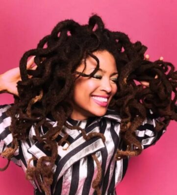Photo of Valerie June wearing a black and white striped top in front of a bright pink background