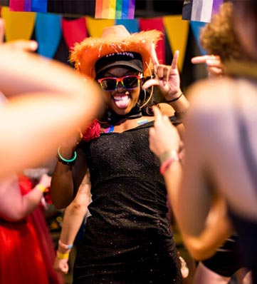 A teen in an orange, feathered cowboy hat makes 'I love you' hand sign to the camera