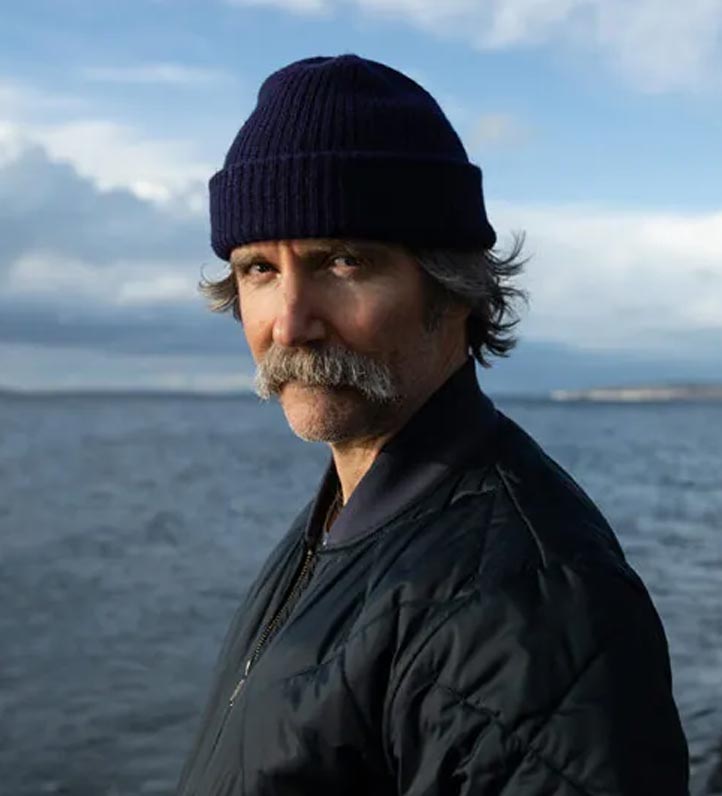photo of Dean Johnson wearing a dark knit cap and quilted jacket standing by a lake