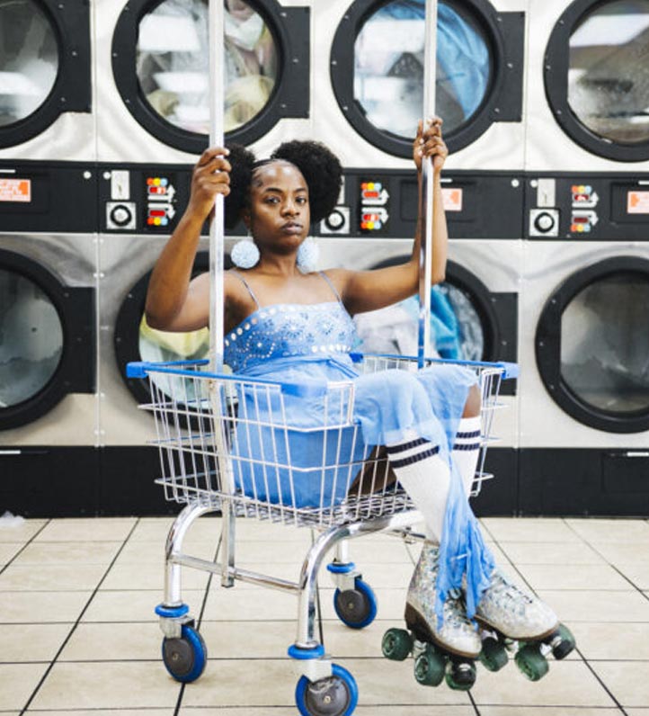 photo of Sunny War wearing a blue skater outfit sitting in a rolling laundry basket while wearing roller skates