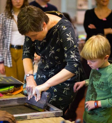 A mother and son squeegee ink onto a silk screen