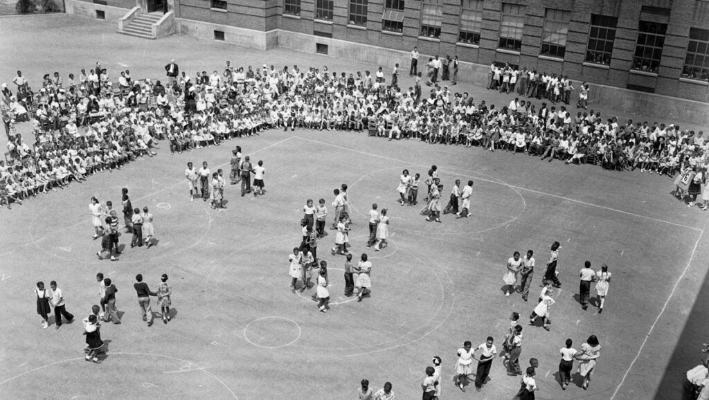 black and white photo of school children giving square dancing demonstration in a school yard