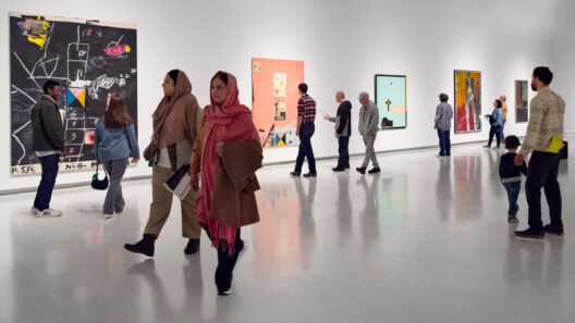 A busy art gallery featuring multiple paintings on the walls, with visitors walking and engaging with the artwork.