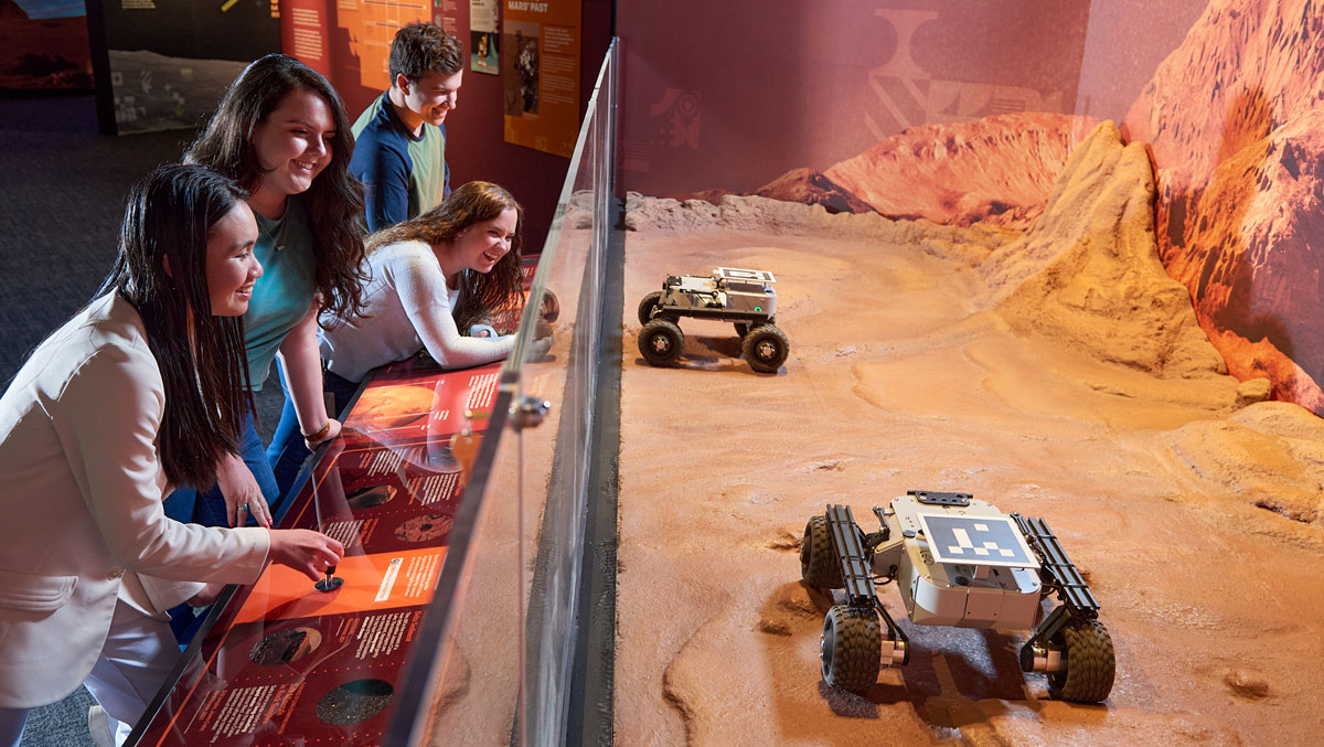 Visitors engage with displays featuring robotic vehicles on a simulated Martian landscape in a museum exhibition.