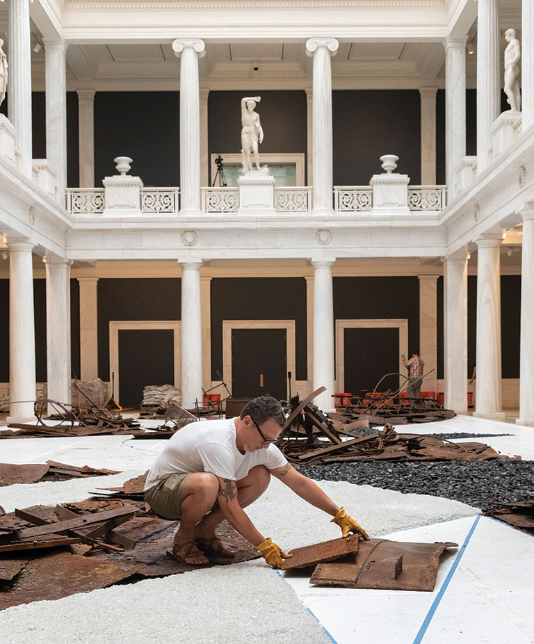 Man squating and working on an installation of artwork in the Hall of Sculpture.
