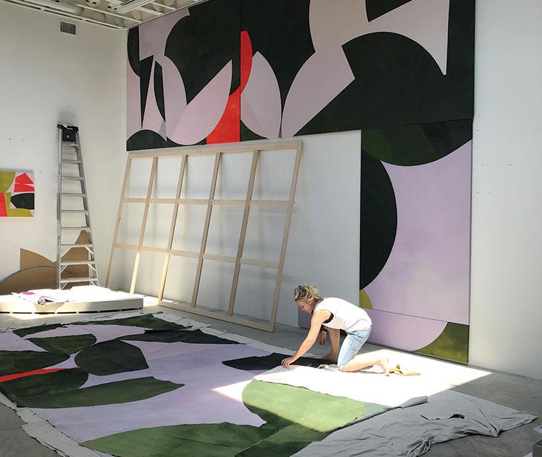 Artist working on a large canvas on the floor of her studio.