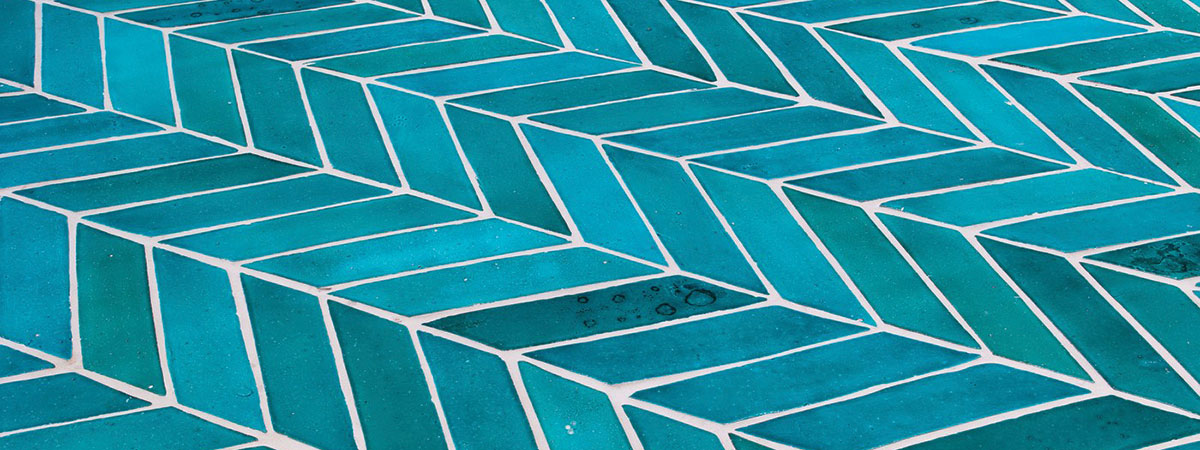 close-up view of blue terra cotta tile laid in a herring bone pattern.