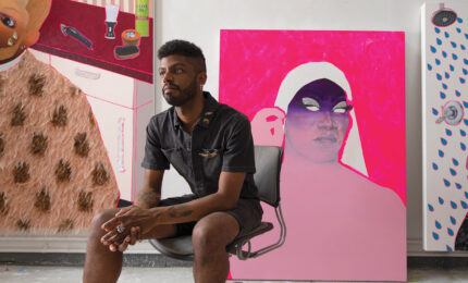 Devan Shimoyama sitting in his studio amongst some of his latest paintings.