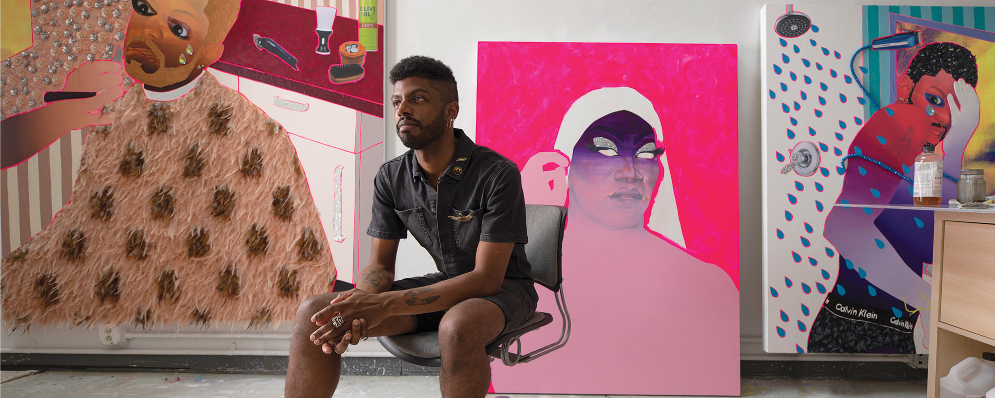 Devan Shimoyama sitting in his studio amongst some of his latest paintings.