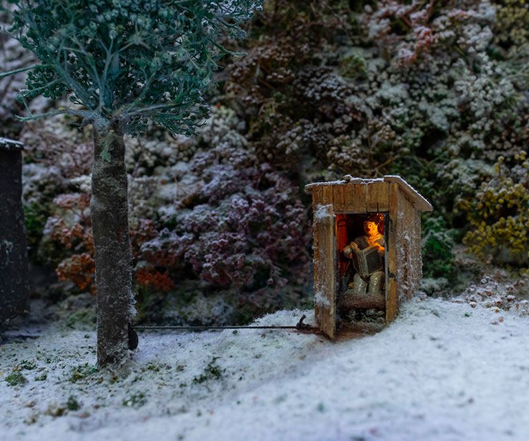 Miniature scene of a man in an outhouse reading a magazine.