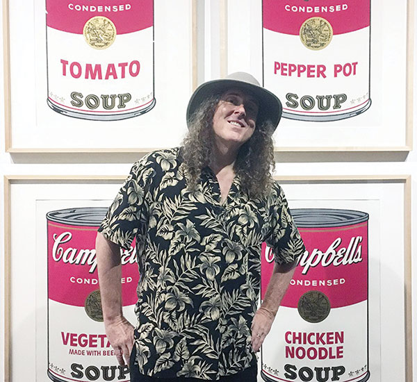 Photo of Weird Al Yankovic at the Warhol Museum standing in front of Warhol's Campbell Soup Cans painting.
