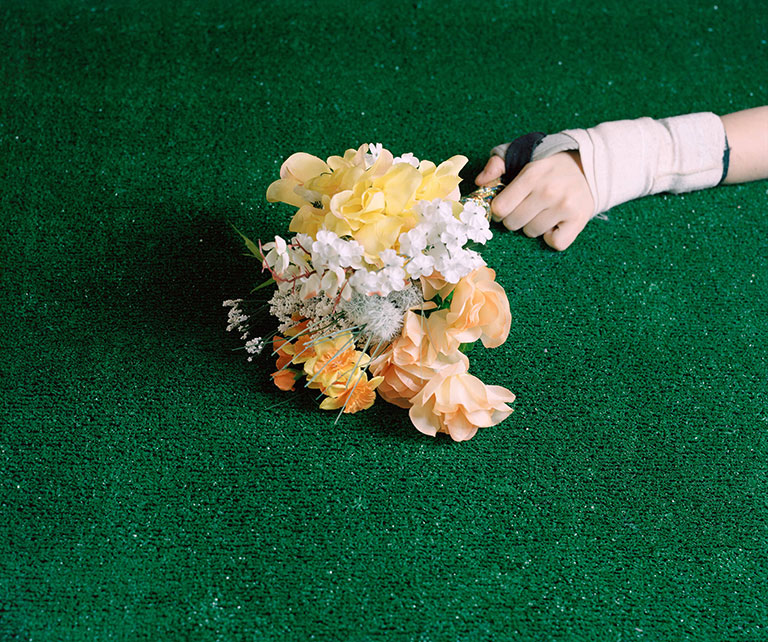 A hand holding artificial flowers laying on artificial turf.