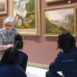 An art docent talking to a group of young students in an art gallery.