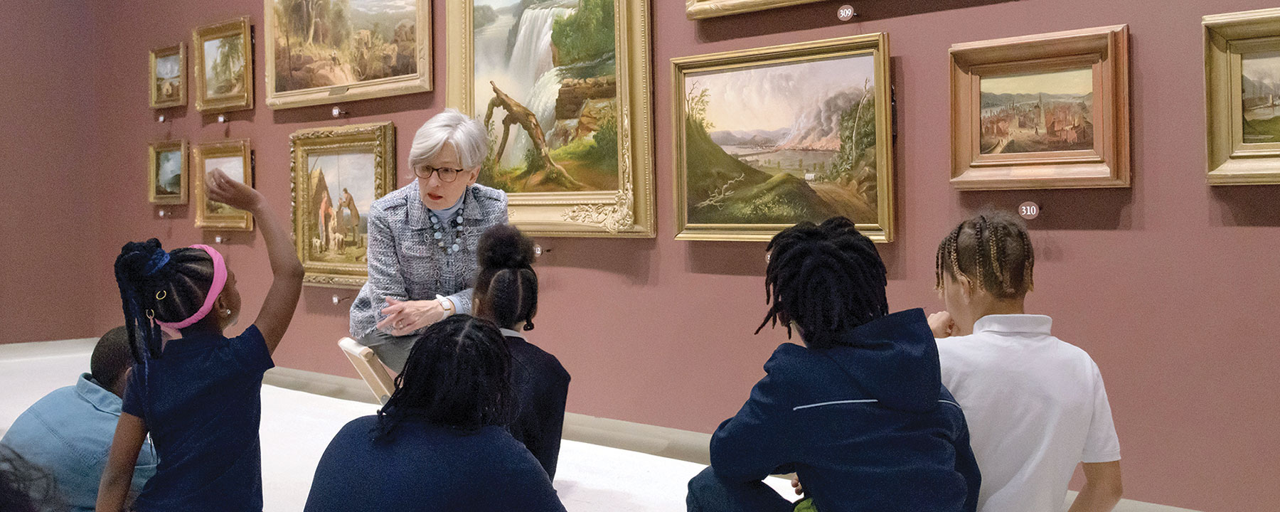 An art docent talking to a group of young students in an art gallery.