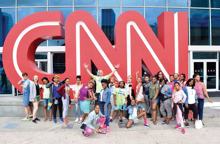 A group of young students standing in front of the CNN sign during a visit to their headquarters.