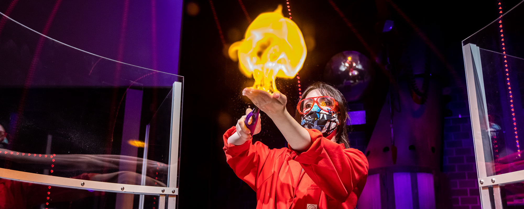 A woman lighting a flame on her hand wearing goggles and a face mask
