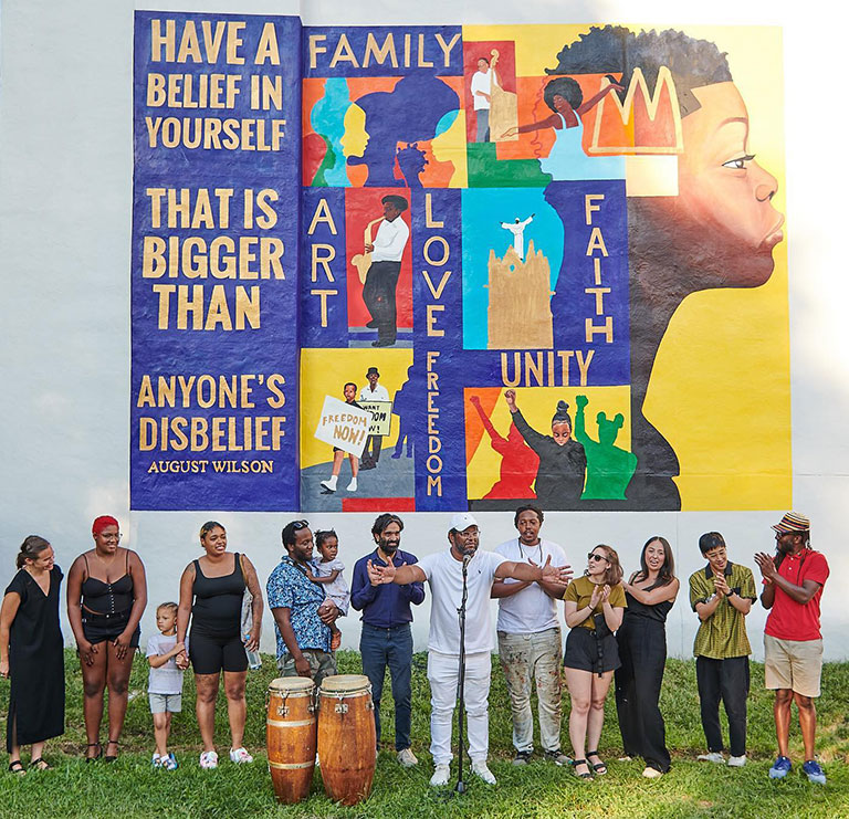 A group of people standing in front of a large wall with a colorful mural