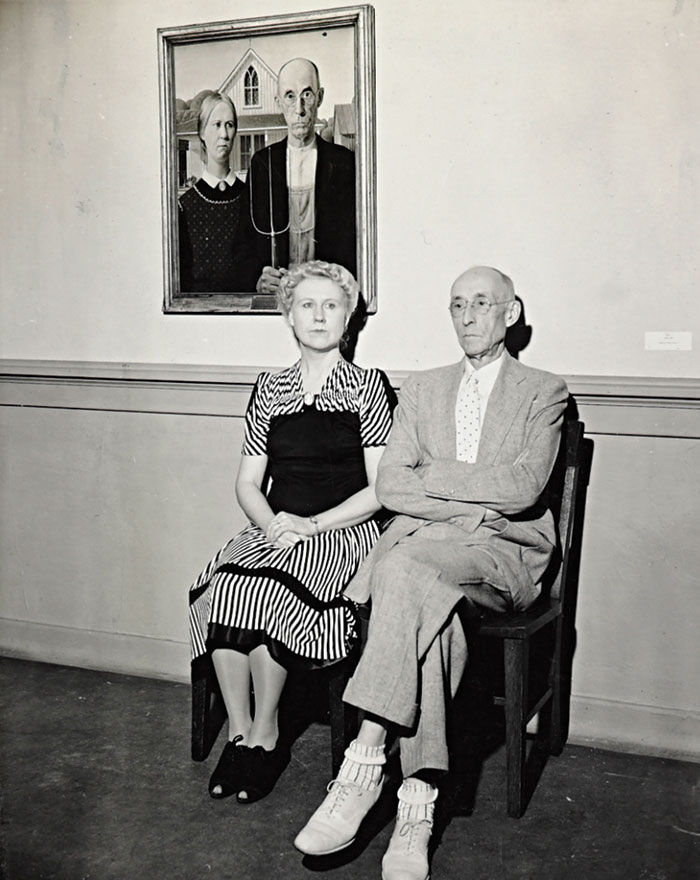 Two people sitting on chairs in front of the American Gothic painting.