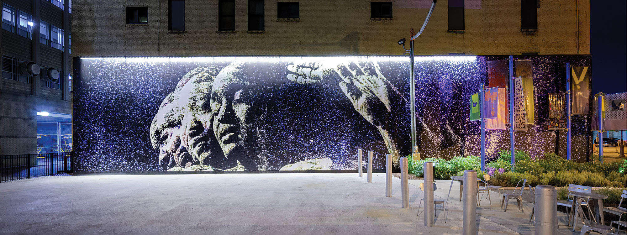 A large mural on the side of a building depicting two figures, side by side with their hands raised.