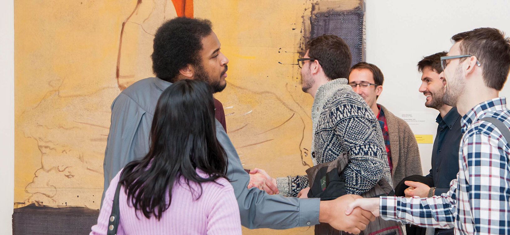 A group of museum-goers greeting each other in front of a large painting in the gallery.